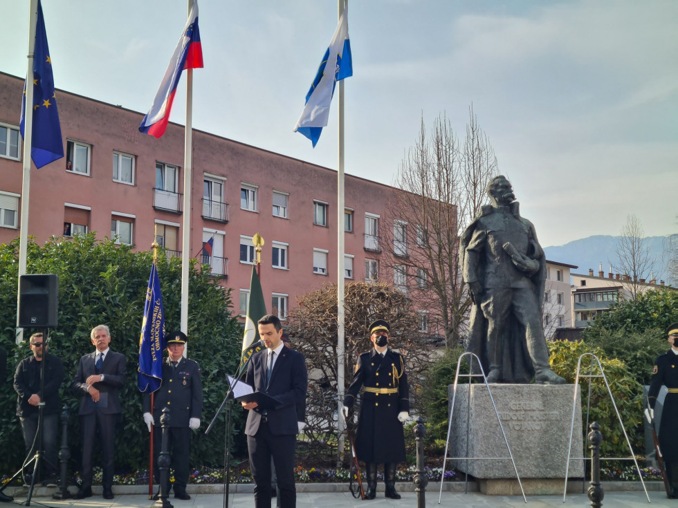 Minister med govorom stoji pred Maistrovim spomenikom. Zadaj stoji gardist in nosilci praporova