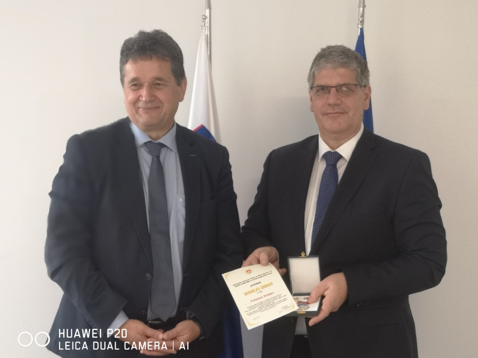 Direktor in predsednik stojita pred zastavama Slovenije in EU, z medaljo in listino
