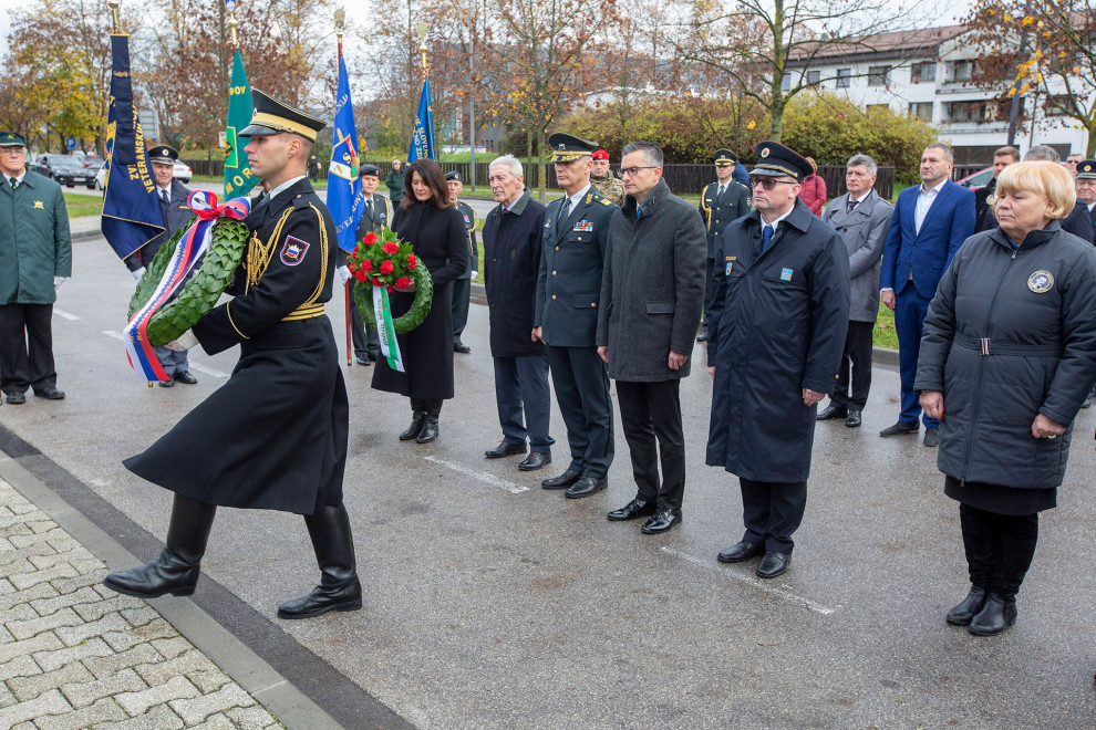 Gardist Slovenske vojske nosi venec. Za njim so minister, načelnik generalštaba in direktor uprave za zaščito in reševanje ter drugi gostje