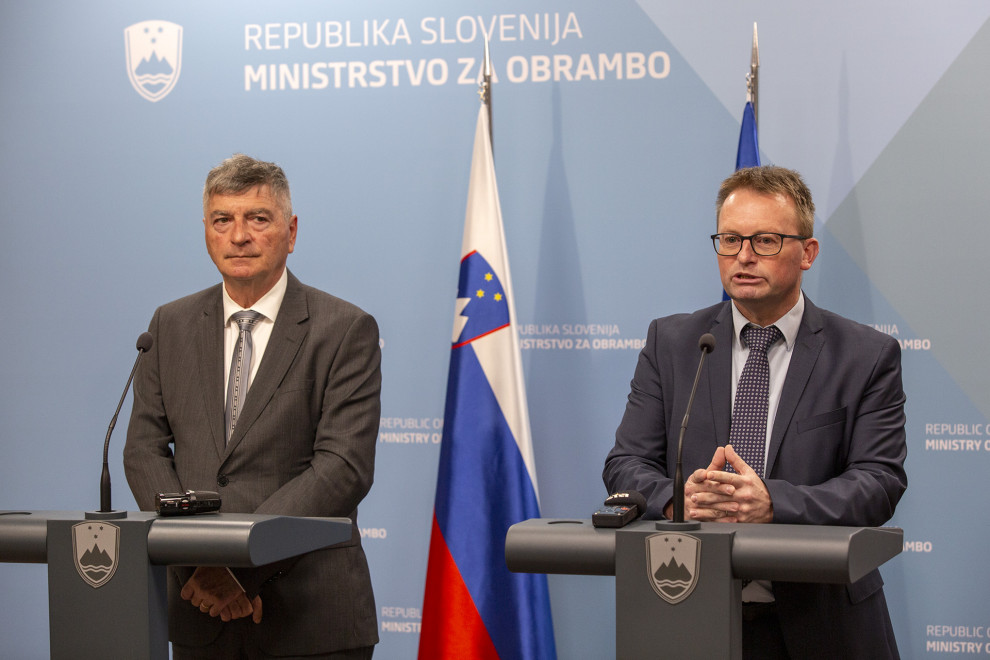 Sekretar in direktor stojita za govornicama. Za njima sta zastavi Slovenije in EU ter moder pano ministrstva