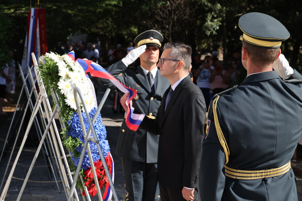 Minister polaga venec ob obeležju v spomin na žrtve nekdanjega taborišča. Ob njem sta gardista.