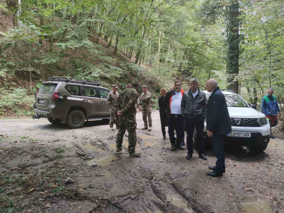 Sekretar in predstavniki lokalne skupnosti stojijo pred avtomobili na poplavnem območju 