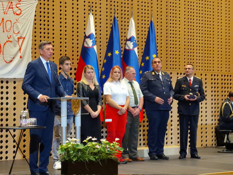 Predsednik stoji za govornico na odru. Poleg stojijo dobitniki priznanj, za njimi so zastave EU in Slovenije