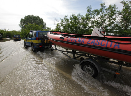 Vozilo Civilne zaščite vleče prikolico s gumenim čolnom po preplavljenem vozišču.
