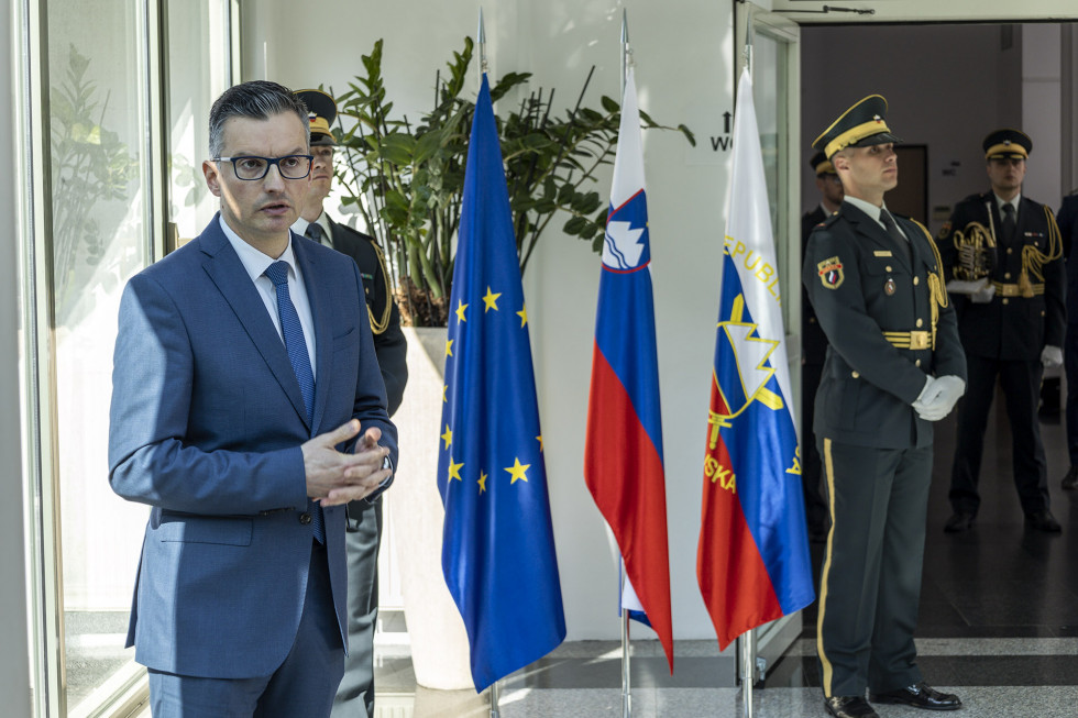 Udeleženci in minister Šarec slovesnosti stojijo ob razstavnih panojih, ki predstavljajo zgodovino slovenske zastave