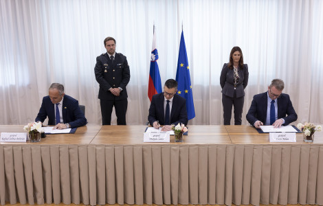 TOIC0959 (Signatories sit at a long table while signing. Behind them are representatives of the Protocol and the flags of Slovenia and the EU)