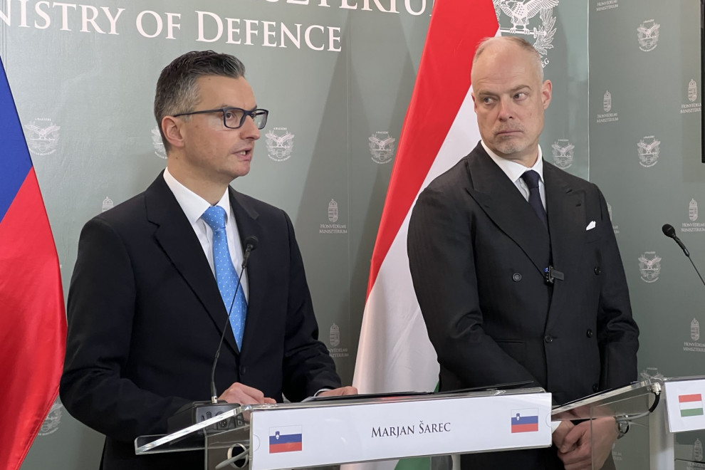 During the statement, the two ministers stand behind lecterns. Behind them is a gray banner of the Ministry and the flags of Slovenia and Hungary