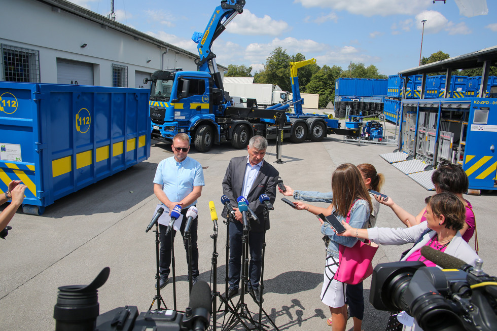 Državni sekretar Medved in vršilec dolžnosti generalnega direktorja Behin stojita pred mikrofoni, v ozadju specialno intervencijsko vozilo