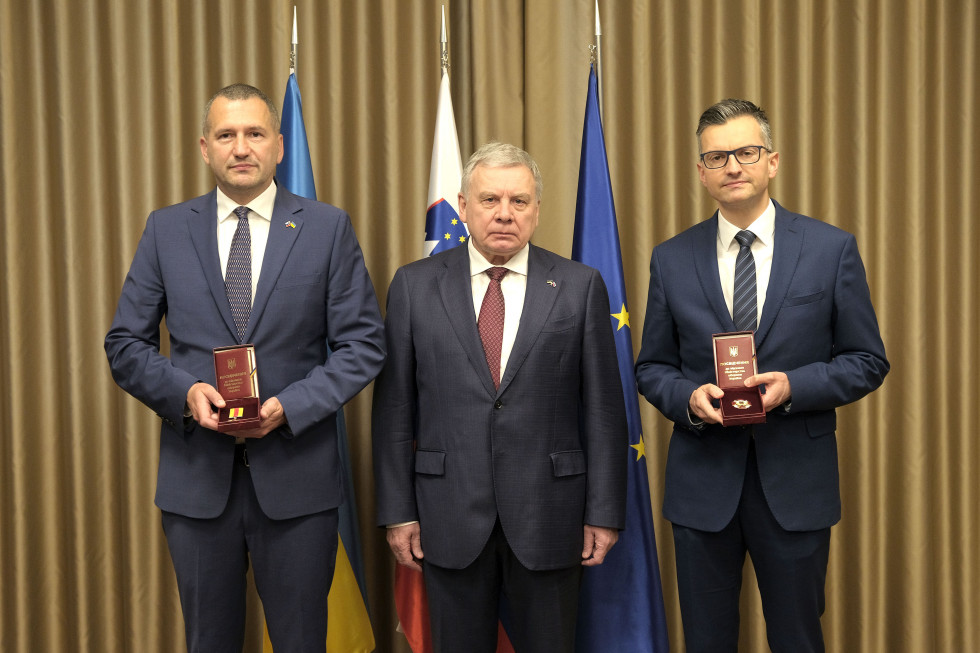 Minister, sekretar in veleposlanik po podelitvi stojijo pred zastavami Ukrajine, Slovenije in EU
