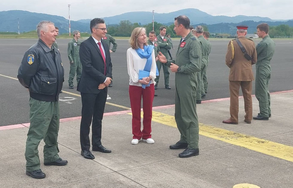 Minister, veleposlanica, predstavnik akrobatske letalske skupine med pogovorom stojijo na letališki stezi v Cerkljah ob Krki