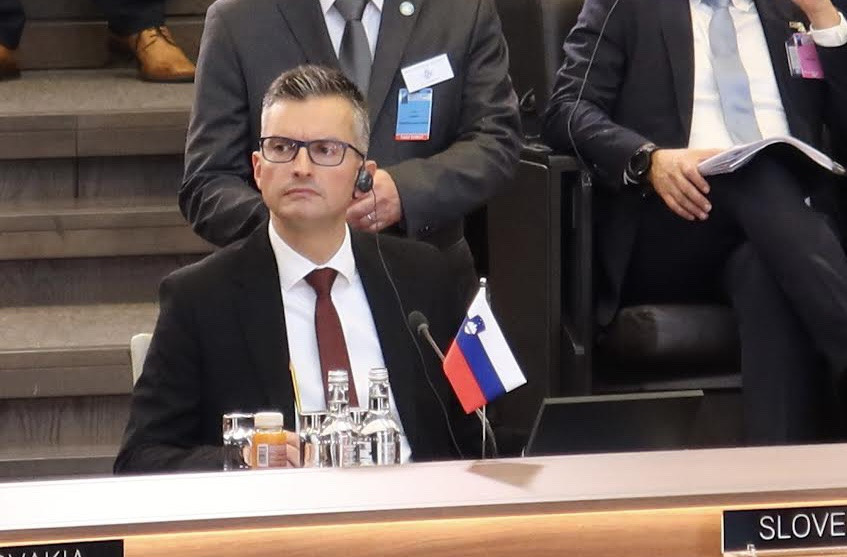Minister med zasedanjem sedi za mizo. Pred njim je slovenska zastavica