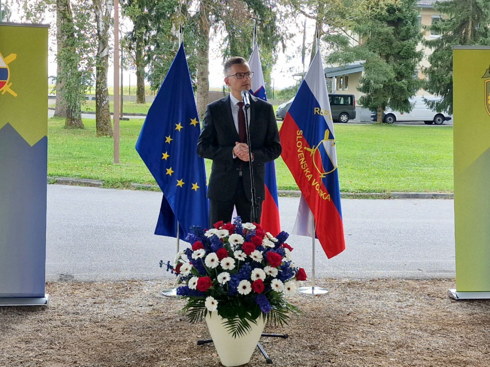 Minister med govorom stoji pred zastavam Slovenije, EU in Slovenske vojske