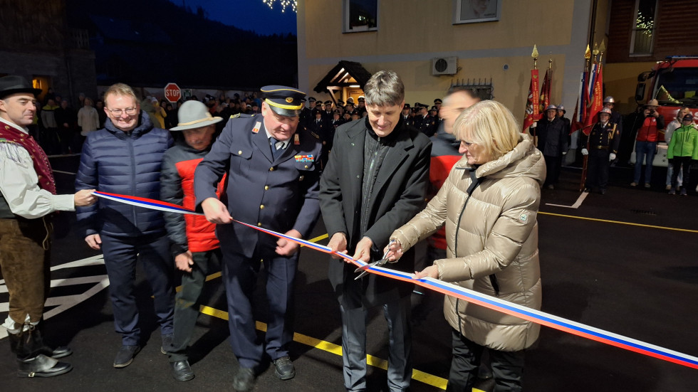 Minister Sajovic in predstavniki gorskih reševalcev in gasilcev režejo trak na slavnostni otvoritvi, v ozadju postroj gasilcev
