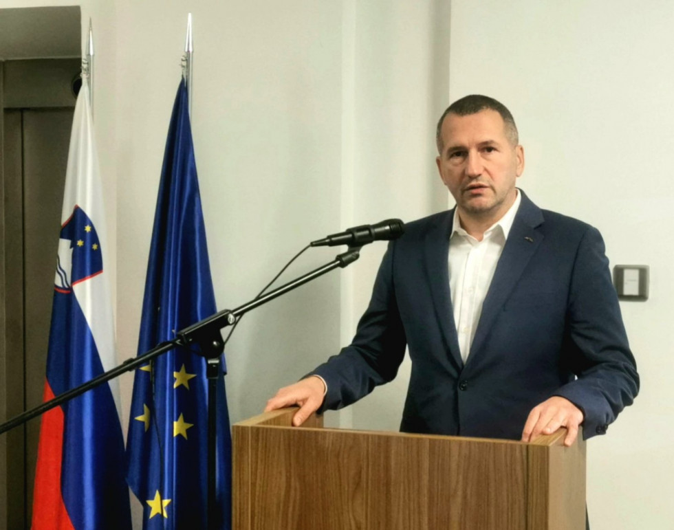 The Secretary stands behind the Speaker during the speech. Behind are the flags of Slovenia and the EU