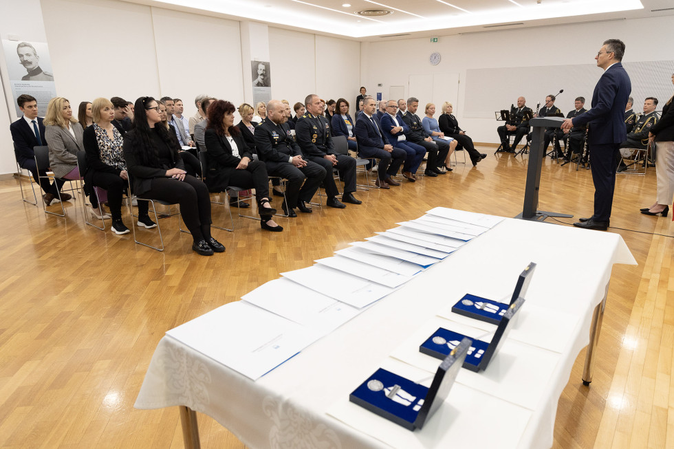 Miza z odlikovanji. V ozadju je minister za govornico in udeleženci, ki sedijo na nasproti.