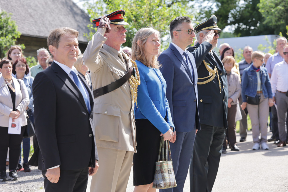 Minister, veleposlanica, župan in drugi gostje stojijo na prostoru pred obeležjem