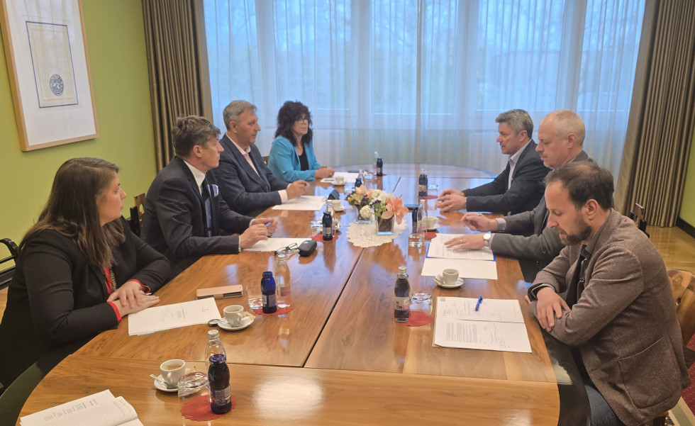 Minister Sajovic s tremi sodelavci in župani sedijo za ovalno konferenčno mizo in se pogovarjajo. V ozadju je z zavesami zastrto okno.