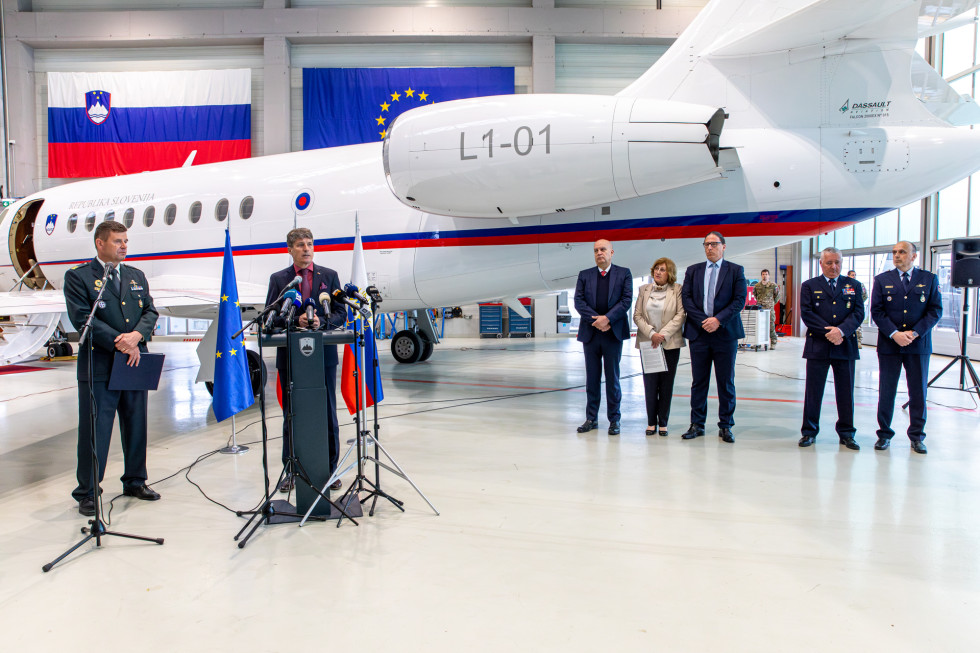 Minister za govornico, za njim pa letalo falcon in predstavniki organizacij, ki sodelujejo pri prevozu organov