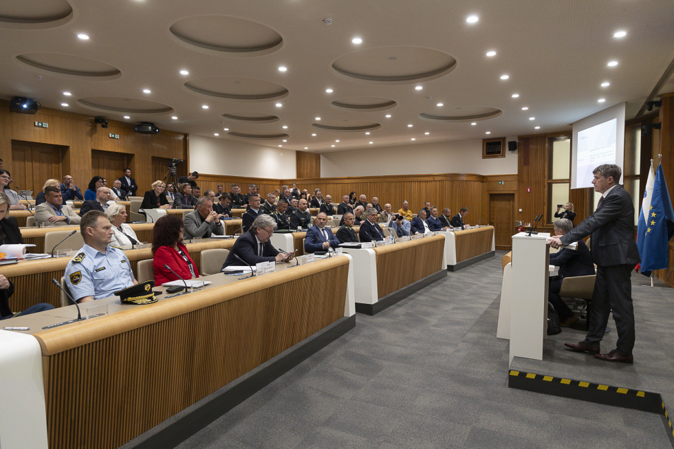 Minister med nagovorom stoji za govornico pred občinstvom v dvorani Državnega sveta