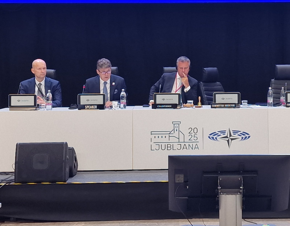 Minister in predsedujoča zasedanju sedijo za mizo na odru. Na belem pregrinjalu mize je logo zasedanja