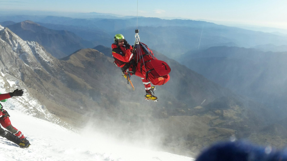 Reševalec z nosili visi na jeklenici pod helikopterjem, ki lebdi nad zasneženim pobočjem