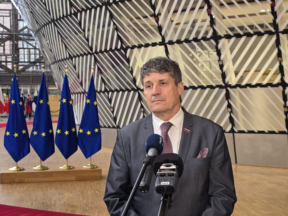 Minister pred mikrofoni med uvodno izjavo. Za njim so zastave EU