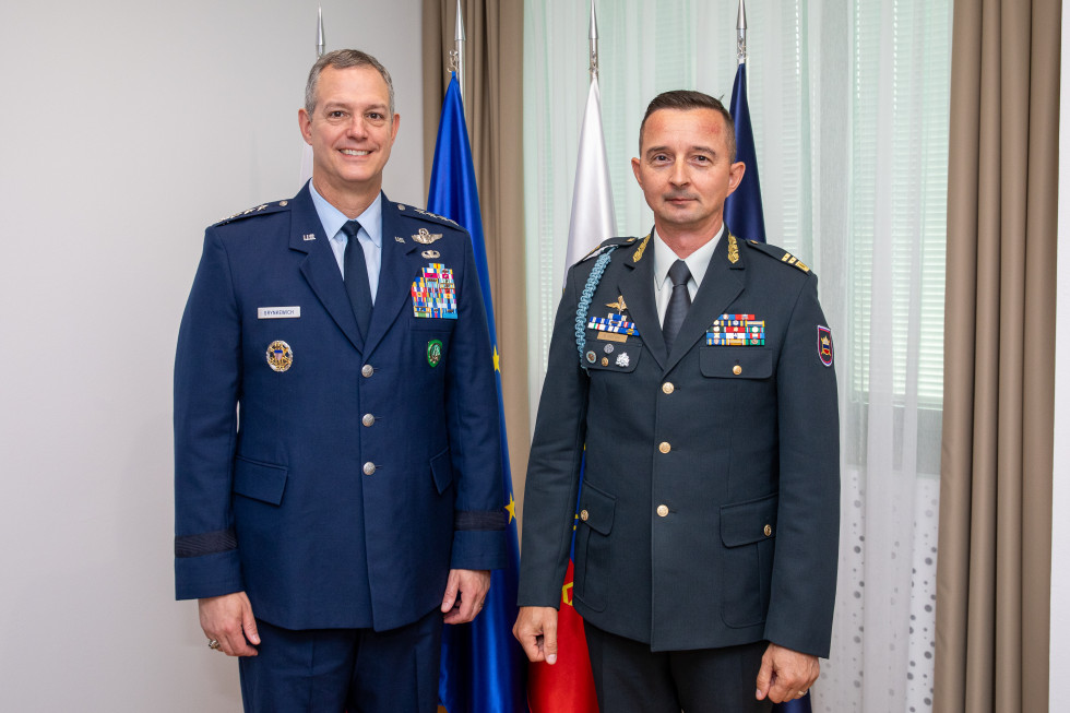 The chief and the general are standing in front of the flags of Slovenia, the EU, and NATO in the reception hall
