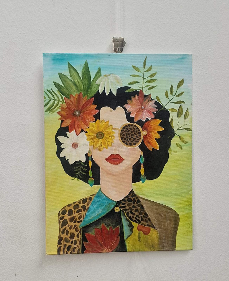 Portret črnolase ženske z bujno pričesko, rožnatimi očali in živo-pisanim cvetjem v laseh z svetlo zelenim in modrim ozadjem.