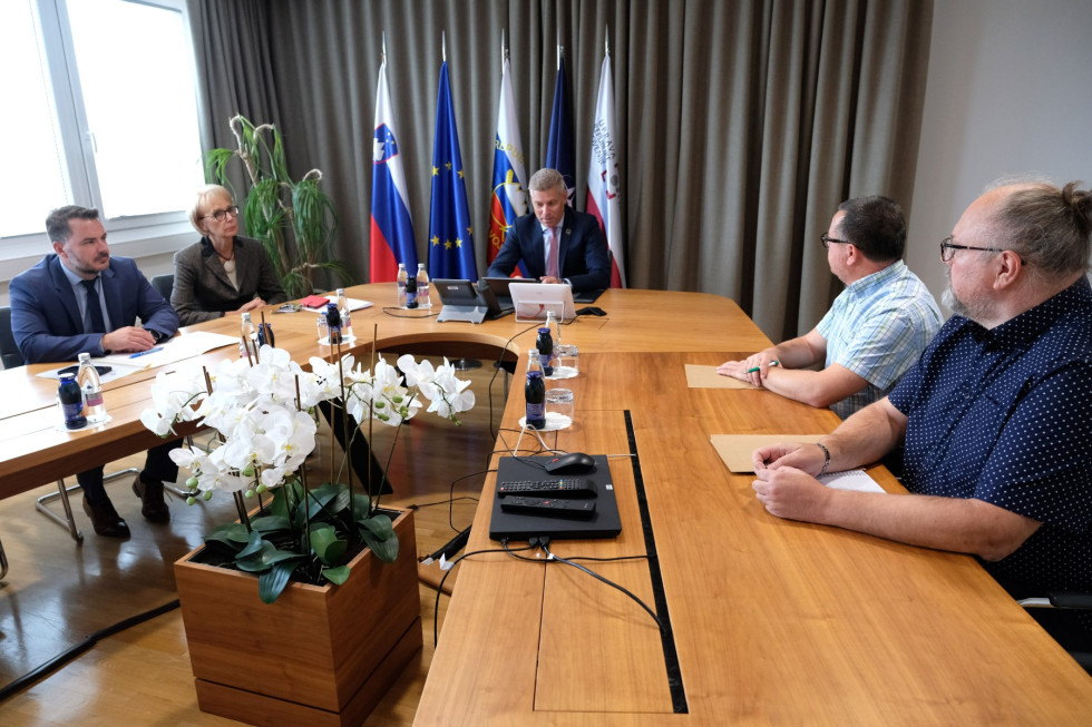 Minister v pogovoru s predstavnikoma sindikata. Za njim so zastave Slovenije, EU in Slovenske vojske.