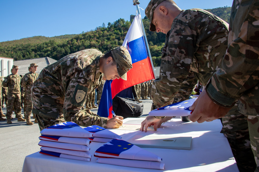 Vojak podpisuje prisego. Za njim je slovenska zastava