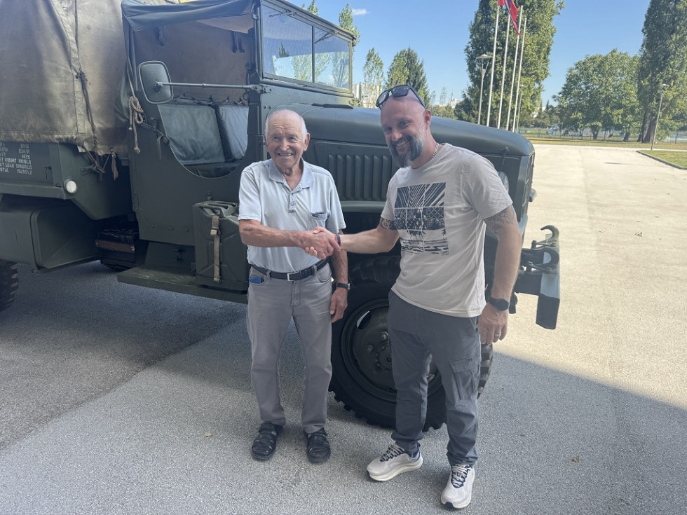 Obiskovalec se rokuje s kustosom pred vozilom GMC 6x6
