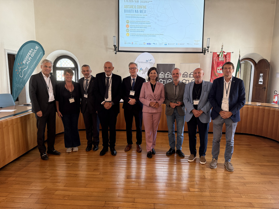 Govorci na konferenci stojijo pred mizami v sejni sobi