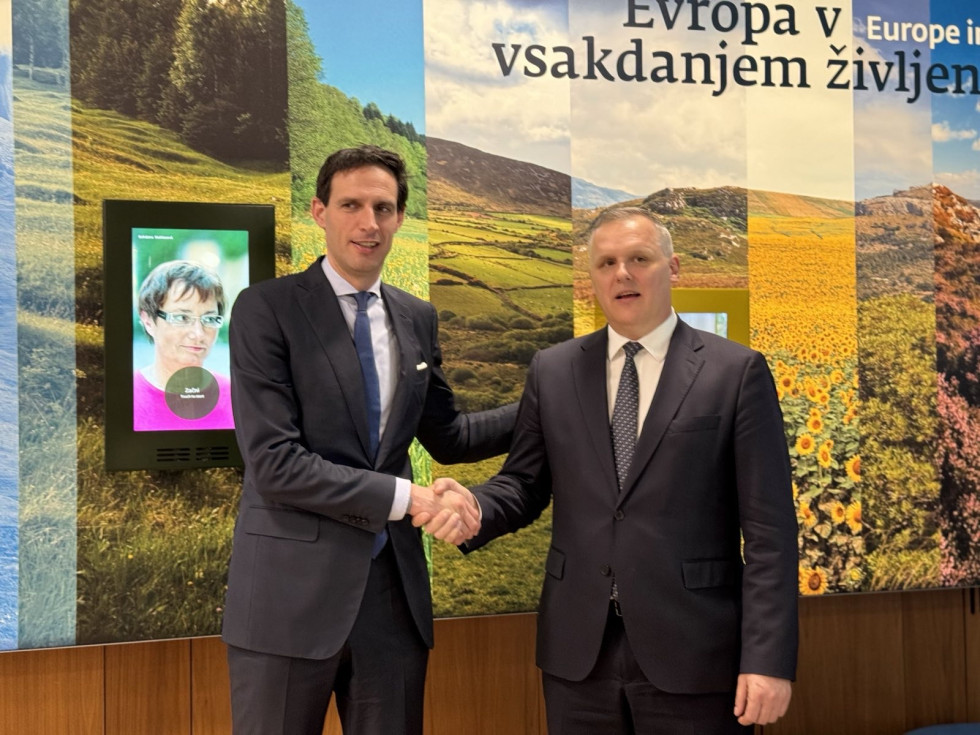 Two men are shaking hands, with a colorful background. The Minister of the Environment, Climate, and Energy, Bojan Kumer, met today with the European Commissioner for Climate Action, Carbon Neutrality, and Clean Growth, Wopke Hoekstra.