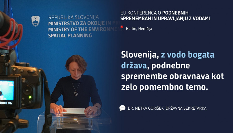 Državna sekretarka za govorniškim pultom. Na fotografiji je tudi napis: Slovenija, z vodo bogata država, podnebne spremembe obravnava kot zelo pomembno temo.