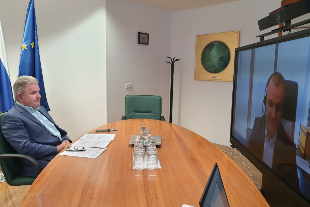 Minister mag. Vizjak sedi za ovalno mizo pred ekranom.