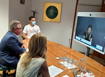 Minister is siting with coleagues behind the desk in front of the television