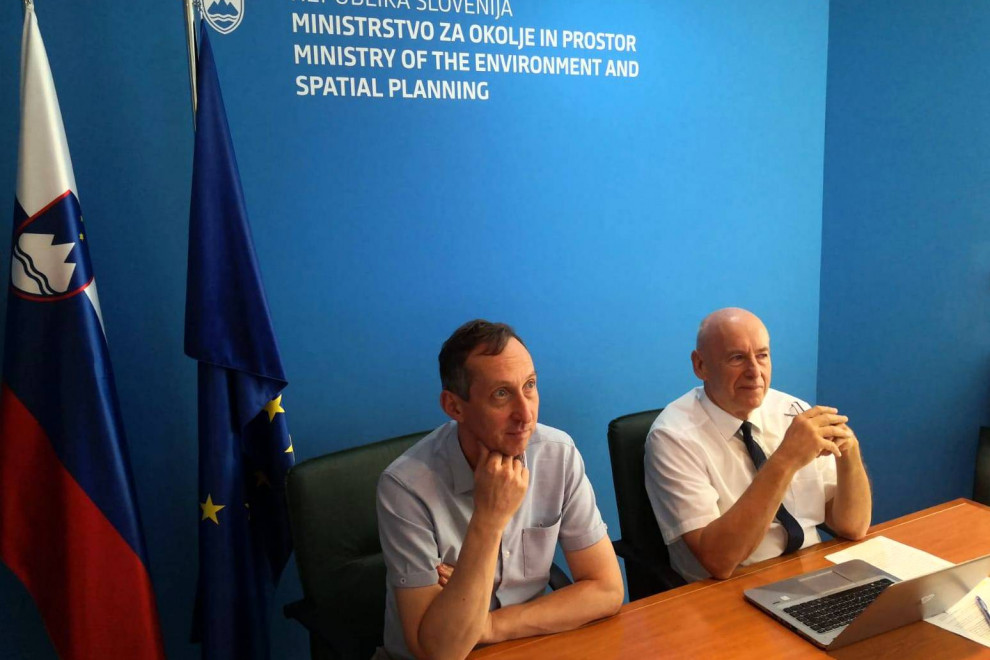 Sogovornika sedita za mizo pred televizijo. Zadaj napis MOP in slovenska ter evropska zastava