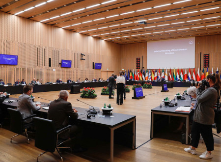 Zasedanje delegacij v dvorani; mize razporejene v kvadrat; zadaj zastave držav EU