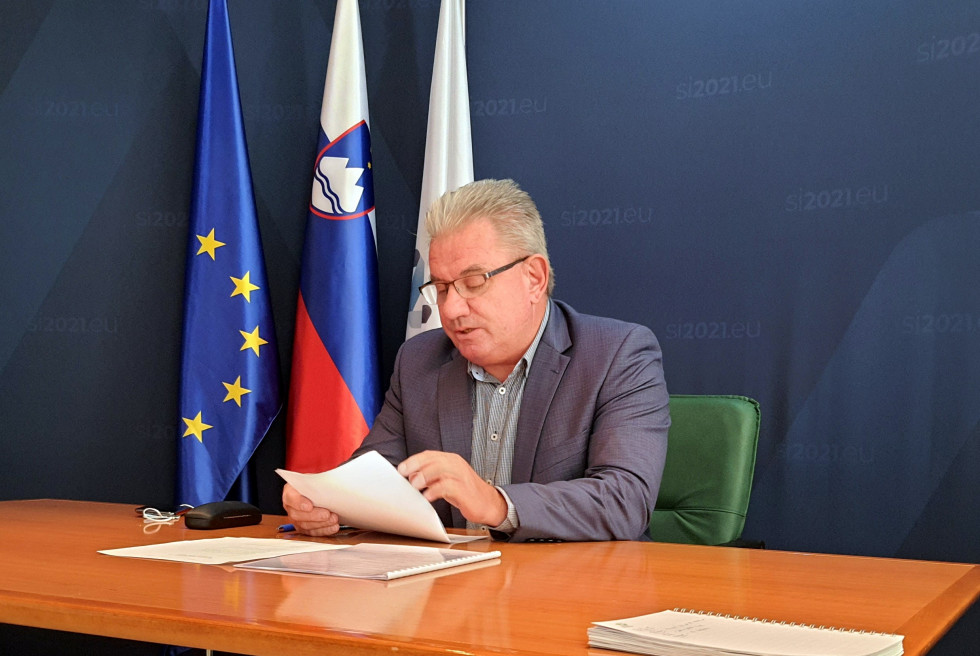Minister sedi za mizo pred zastavami EU, Slovenije in predsedovanja