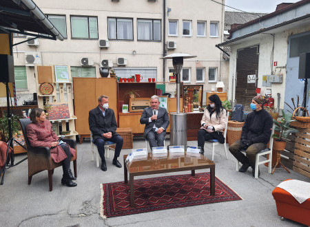 Udeleženci na novinarski konferenci sedijo na stolih, zunaj, v ozadju izdelki iz ponovne uporabe (omare, okvirji, radio, luči) 