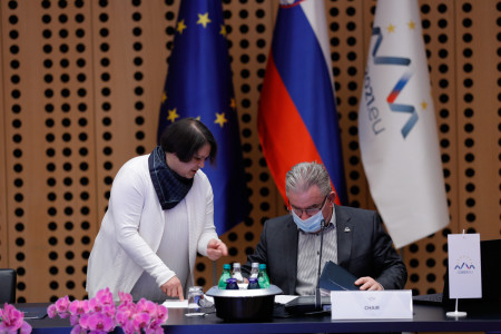 Minister v dvorani sedi za mizo, v pogovoru s sodelavko