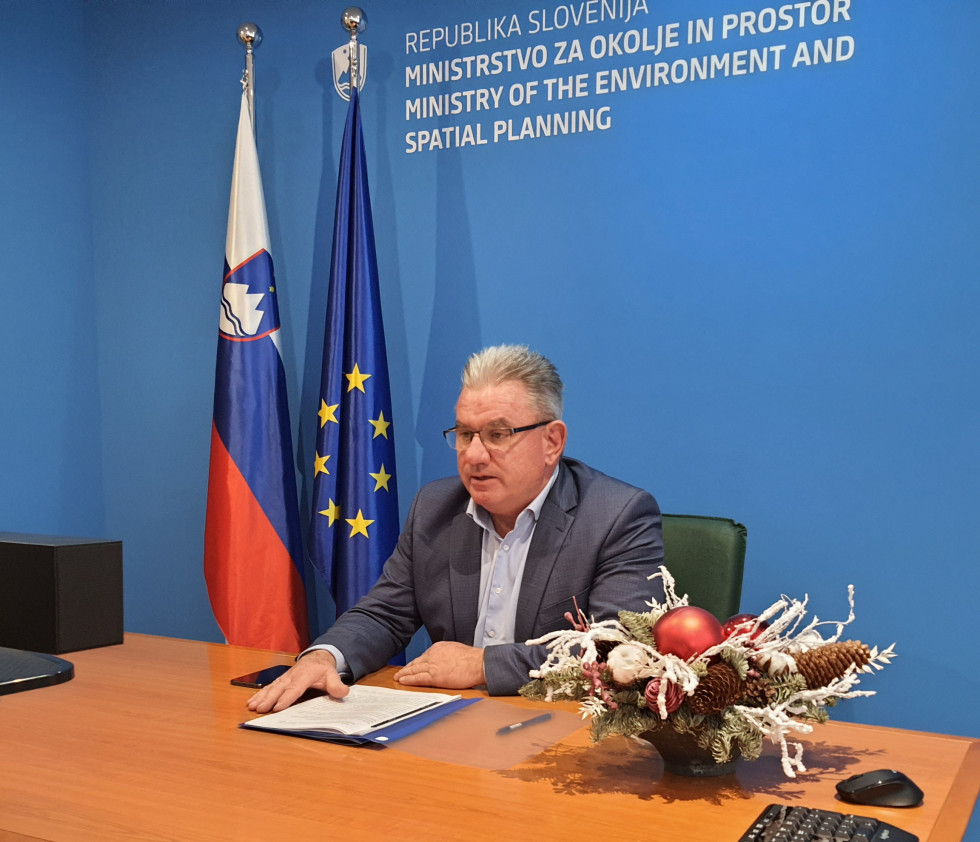 Minister Andrej Vizjak sedi za mizo pred ozadjem MOP in slovensko ter EU zastavo