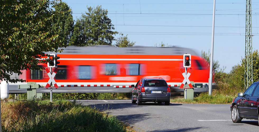 Slika avta pred zaprtim železniškim prehodom z vlakom, ki pelje mimo 