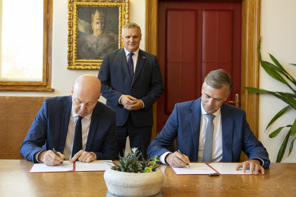 minister, ki stoji za dvema moškima, ki podpisujeta pogodbo