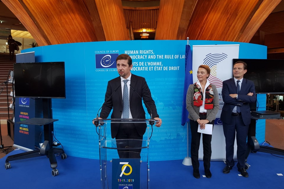 G. Strojin pred modrim uradnim ozadjem odgovarja na vprašanje.