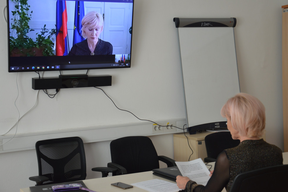 Ministrica Lilijana Kozlovič sedi za mizo in sodeluje na video konferenci