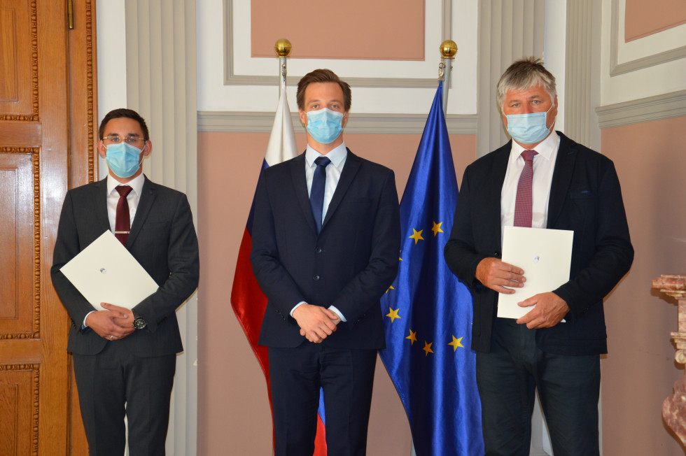 Novozaprisežena izvršitelja Tomaž Mijailović in Uroš Nikolaj Pavkovič ter državni sekretar Zlatko Ratej stoji pred zastavami