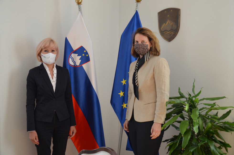 Ministrica mag. Lilijana Kozlovič in avstrijska veleposlanica v Sloveniji Elisabeth Ellison-Kramer stojita pred zastavami