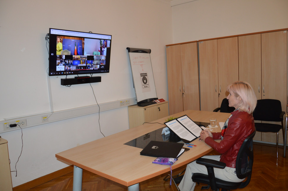 Ministrica mag. Lilijana Kozlovič sedi za mizo in sodeluje na zasedanju prek video konference