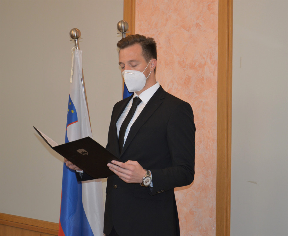 Državni sekretar Zlatko Ratej stoji, v roki drži mapo z govorov ob zaprisegi sodnih izvedencev, cenilcev in tolmačke